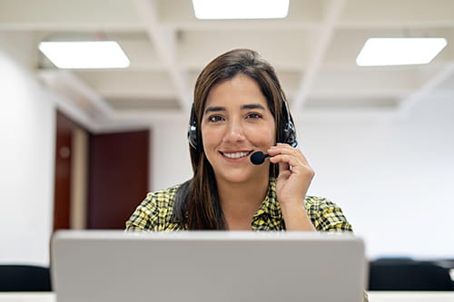 Smiling employee holds her headset microphone close to her mouth while looking over the top of her laptop